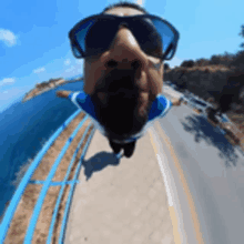 a man wearing sunglasses is hanging upside down on a bridge overlooking the ocean