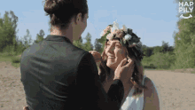 a bride and groom are looking at each other and the bride is wearing a flower crown on her head .