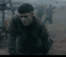 a man is kneeling down in the dirt in a field with a group of people in the background .