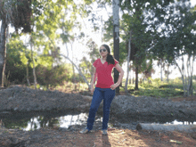 a woman wearing sunglasses and a red shirt stands in front of a river