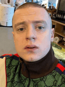 a man with a shaved head is wearing a green and brown sweater and a turtleneck .