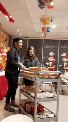 a man and a woman standing in front of a cart of food with a sign that says dance above them