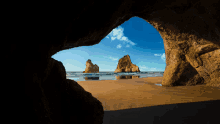 a view of a beach from a cave with rocks in the foreground