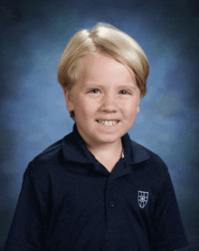 a young boy wearing a blue polo shirt with a shield on the front