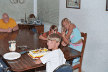 a group of children sit around a table with a birthday cake on it