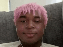 a young man with pink hair is sitting on a couch wearing headphones .