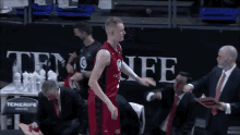 a man in a red and black basketball uniform stands in front of a sign that says tenerife on it