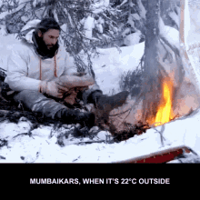 a man sits in the snow near a fire with the words " mumbaikars when it 's 22 degrees outside " below him