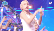 a woman in a white dress is dancing on a stage in front of a sign that says ' mnet ' on it