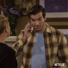 a man in a plaid shirt is talking on a cell phone with netflix written on the bottom right