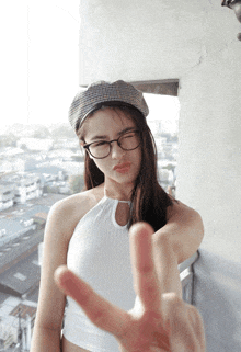 a woman wearing glasses and a hat is making a peace sign with her hand