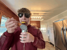 a man wearing sunglasses is eating corn from a can with a spoon