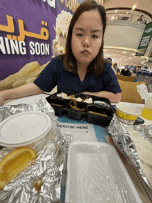 a woman sits at a table with food and a sign that says ' advertising here ' on it