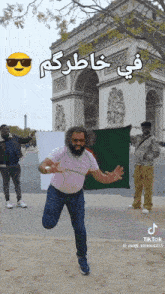 a man in a pink shirt is jumping in the air while holding a green flag in front of the triumphal arch