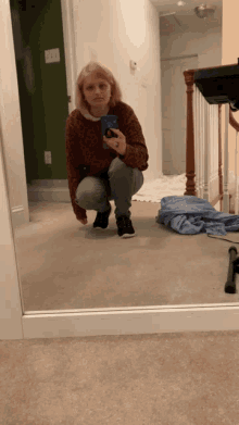 a woman is squatting down in front of a mirror taking a picture of herself