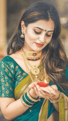 a woman wearing a green blouse and gold jewelry is holding a candle in her hand