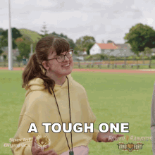 a girl in a yellow hoodie is smiling and holding a donut with the words a tough one on it