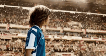 a young boy in a blue and white jersey is standing in front of a crowd of people at a soccer game .