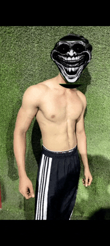 a shirtless man wearing a troll mask and adidas shorts