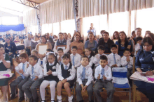 a group of children in school uniforms are sitting in a room with their parents