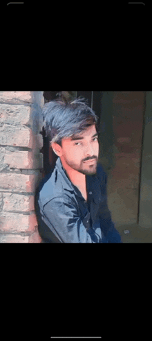 a young man is leaning against a brick wall and looking at the camera .