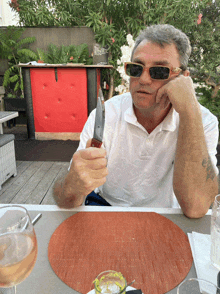 a man wearing sunglasses sits at a table holding a large knife