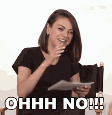 a woman in a black shirt is sitting in a chair holding a piece of paper and laughing .