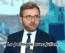 a man in a suit and tie is standing in front of a microphone with the words la politique avec julien written above him .