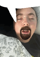 a man with glasses and a beard is laying on a bed