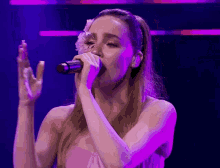 a woman singing into a microphone with purple lights behind her