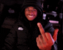 a man wearing a black jacket with a white nike logo on the front is giving the middle finger