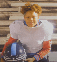 a young man in a football uniform sits on a bench holding a football helmet