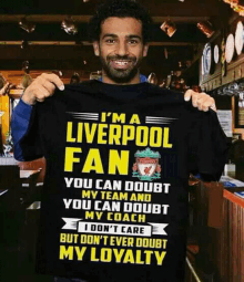 a man is holding up a liverpool fan t-shirt