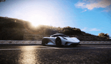 a white sports car is driving down a road with the sun shining brightly behind it