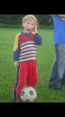 a young boy standing next to a soccer ball and talking on a cell phone