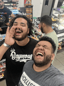 a man wearing a hollister shirt laughs with another man wearing a raymours shirt