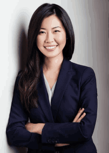 a woman in a blue suit is smiling with her arms crossed .