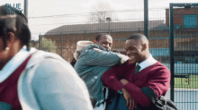 a group of young men are hugging each other in front of a fence with blue story written on it