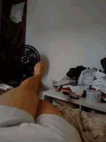 a person laying on a bed with their feet up and a fan in the background