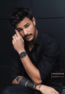 a man wearing a black shirt and a watch has a tattoo on his arm