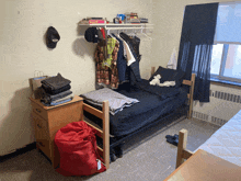 a bedroom with a bed and a shelf with clothes on it and a bag of clothes on the floor that has a tag on it