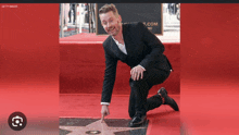 a man in a suit is kneeling down on a red carpet and pointing at a star