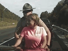 a man in a ranger hat is holding a woman in a pink shirt on the back of a car .