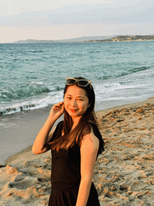 a woman wearing sunglasses stands on a sandy beach