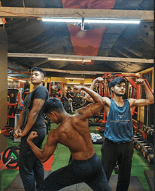 a man with a blue tank top that says ' reebok ' on it flexes his muscles in a gym