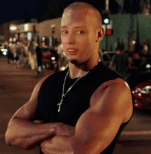 a man with his arms crossed wears a black tank top and a cross necklace