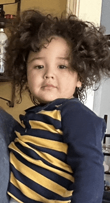 a young boy with curly hair is wearing a blue and yellow striped shirt