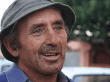 a man wearing a hat and a blue shirt smiles for the camera