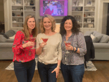 three women holding up martini glasses in front of a television