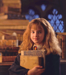 a young girl is holding a stack of books